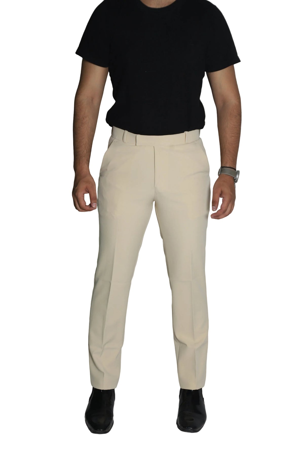 A man wearing off-white tailored trousers, a black short-sleeve t-shirt, and black shoes, standing against a solid beige background.